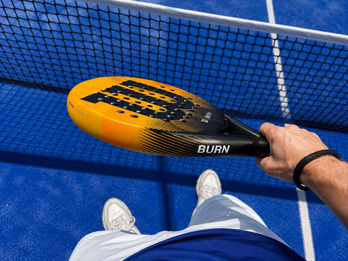 Raquette de padel tenue en main au-dessus du filet sur un terrain bleu