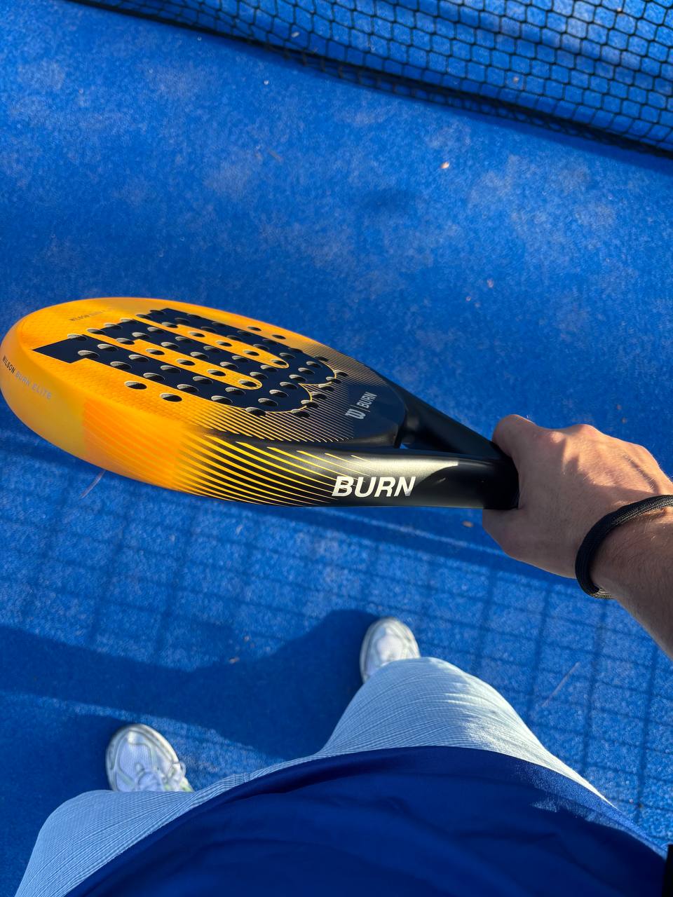 Forme d'une raquette de padel tenue en main sur un terrain de padel