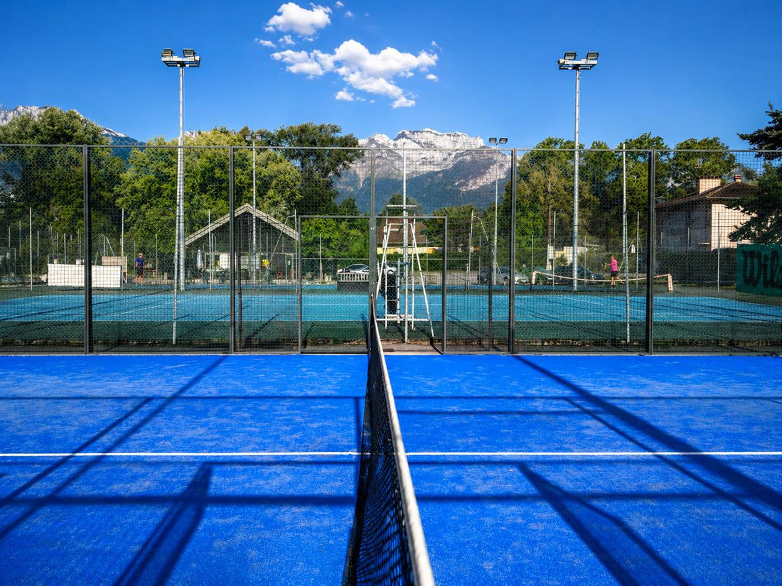 Terrain de padel bleu en extérieur avec filet et montagnes en arrière-plan
