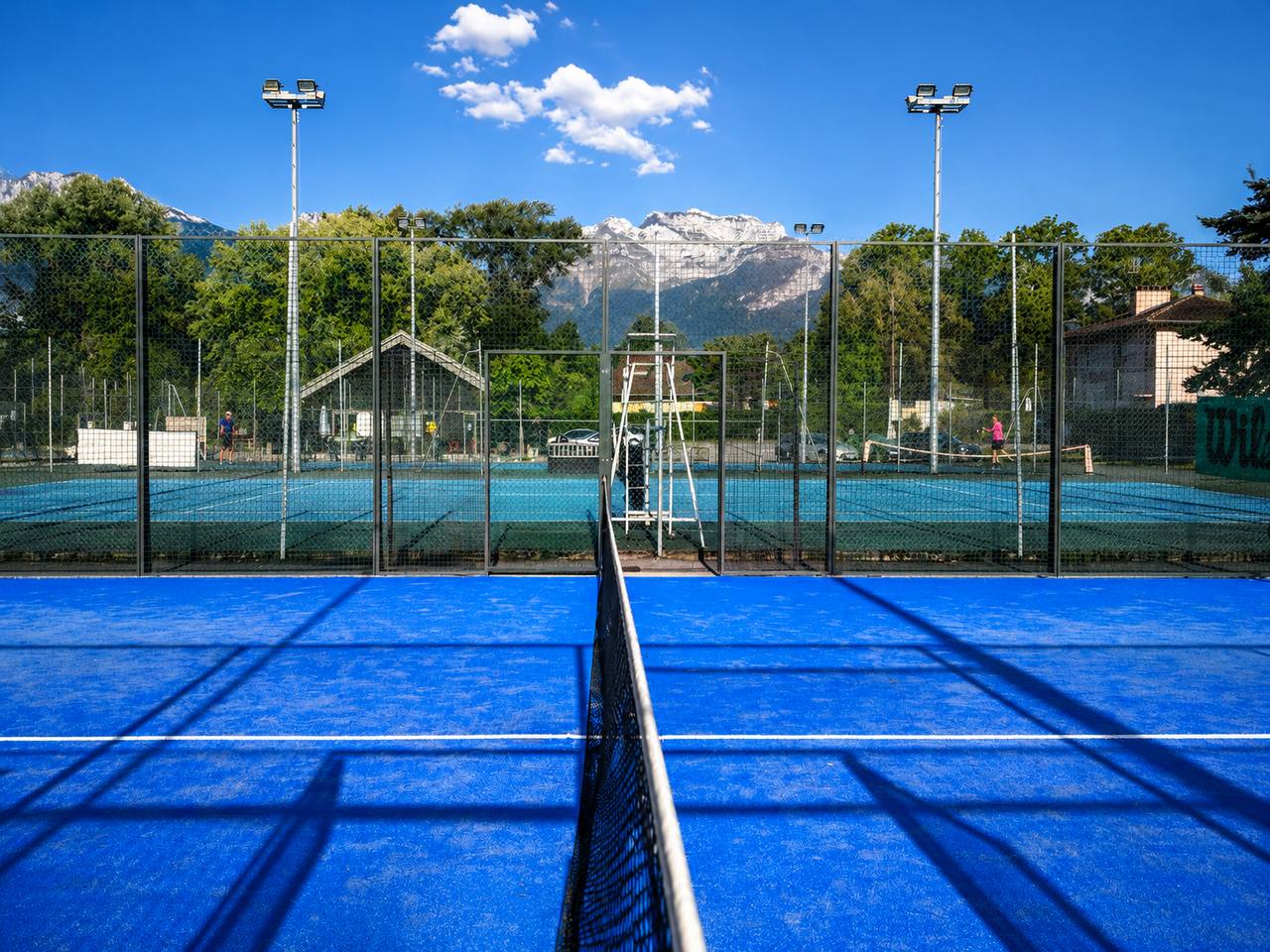Terrain de padel bleu en extérieur avec filet et montagnes en arrière-plan