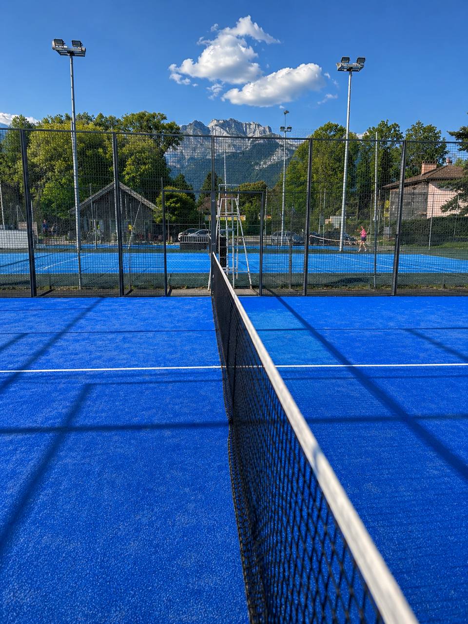 Terrain de padel extérieur bleu avec filet au premier plan et montagnes en arrière-plan